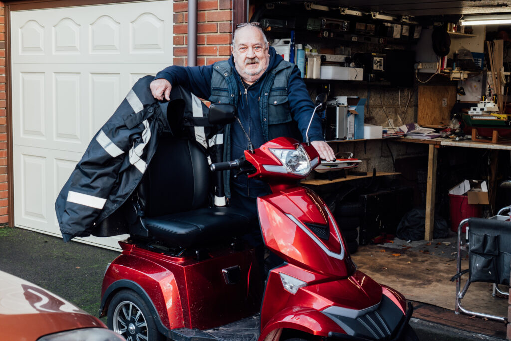 Person standing beside a red mobility scooter in a garage while checking equipment and accessories.